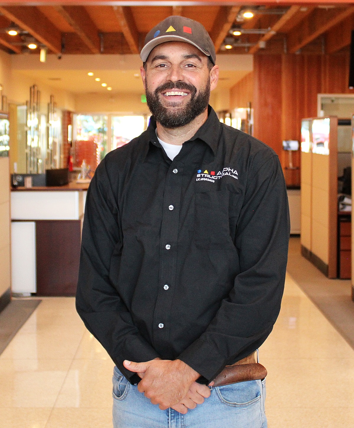 Man smiling in a business setting, wearing a cap.