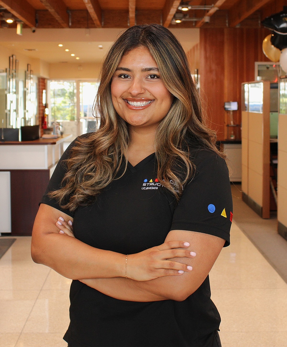 Smiling woman in black polo shirt, arms crossed.