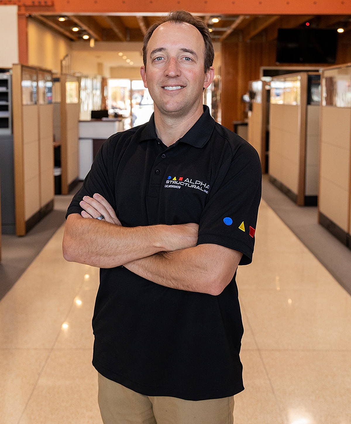 Man in a black polo standing confidently indoors.