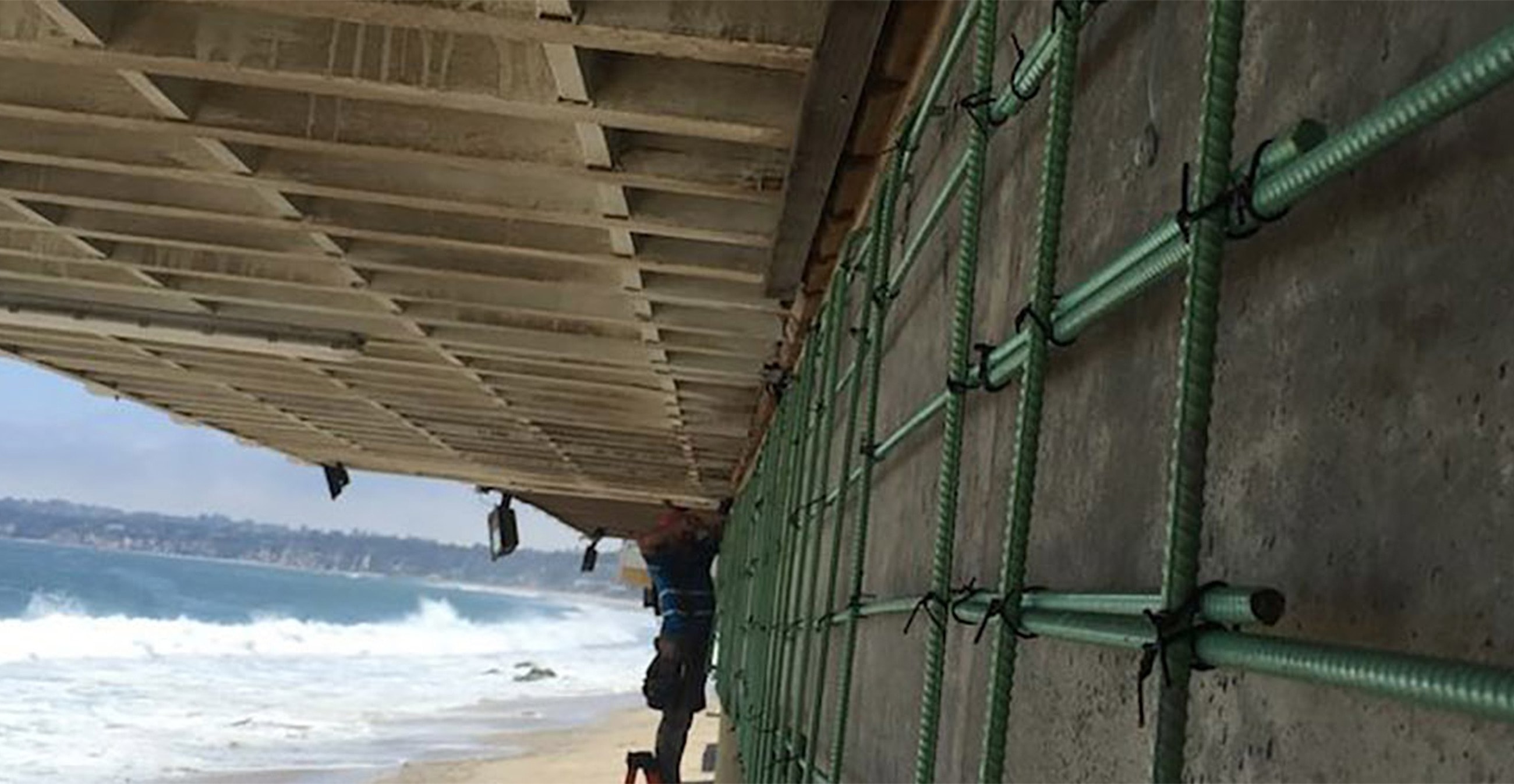 Worker repairing structure under beachside bridge.