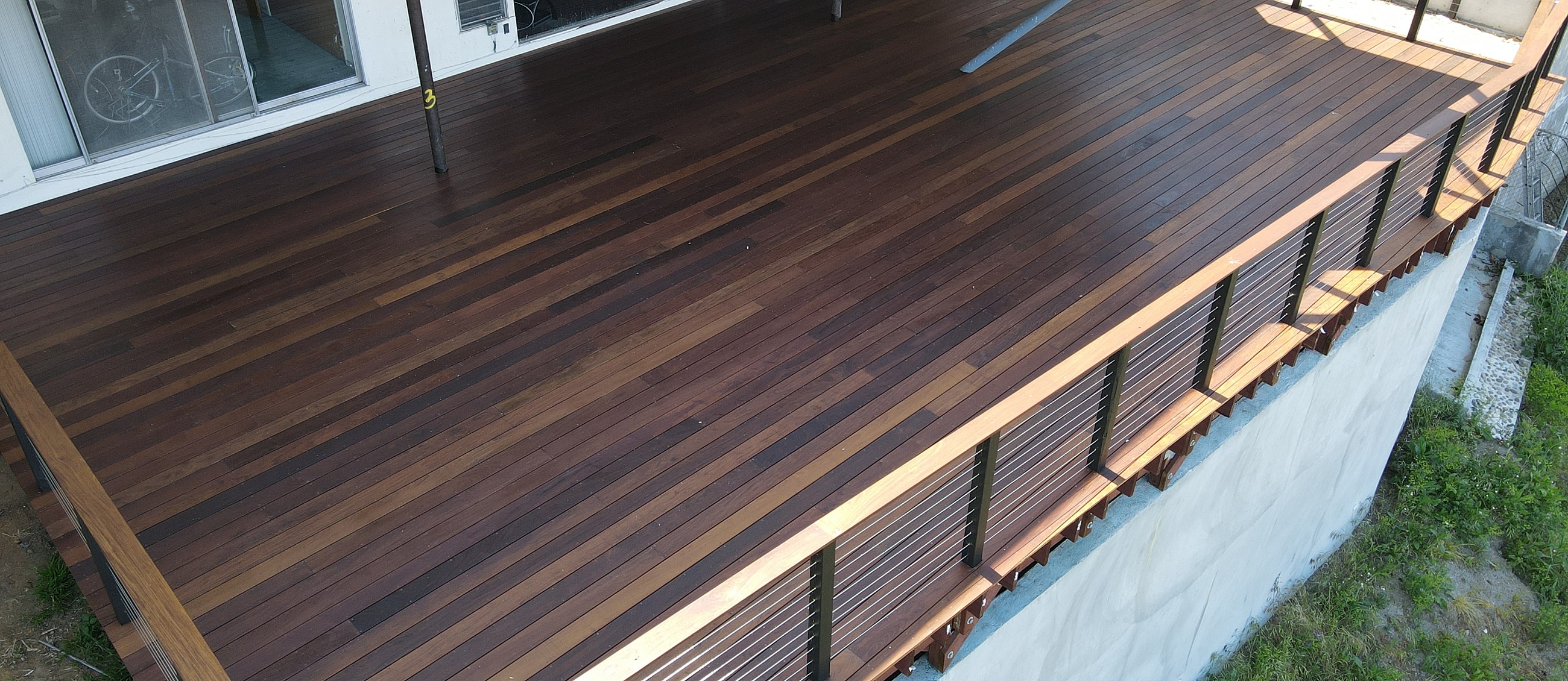 Wooden deck with modern railing and shadows.